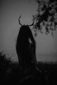 a woman with long hair and horns sitting in the grass under a tree at night