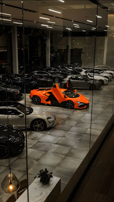 an orange sports car in a showroom with other cars behind the glass wall and on the floor