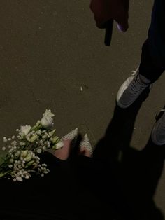 a person standing next to a bouquet of flowers on the ground with their feet in the air