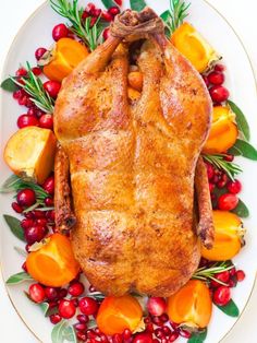 a roasted turkey on a platter with cranberries, oranges and greenery