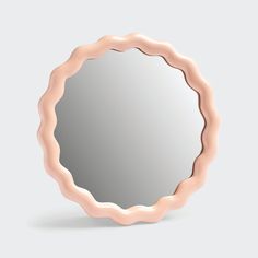 a round mirror with wavy edges on a gray background, it is reflecting the light