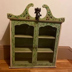 an old green painted china cabinet with a figurine sitting on top of it