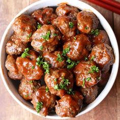 a white bowl filled with meatballs next to chopsticks on a wooden table