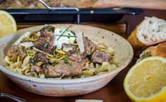 a bowl filled with pasta and meat next to sliced lemons