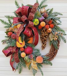 a wreath with fruit and greenery hanging on the side of a door, decorated with red ribbon