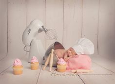 a baby laying on top of a pink blanket next to cupcakes and a mixer