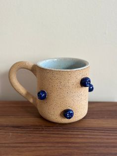 a coffee cup with blue balls on it sitting on a wooden table next to a white wall