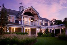 a large house with lots of windows and lights on it's front porch at dusk