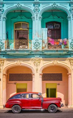 an old red car is parked in front of a colorful building with balconies