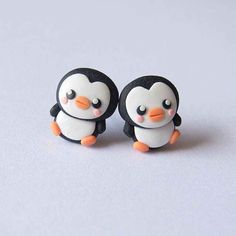 two little penguins sitting next to each other on top of a white surface with one penguin looking at the camera