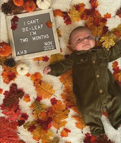 a baby laying on top of leaves next to a sign that says i can't be leaf two months ago