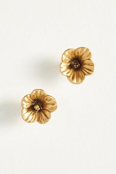 two gold flower shaped earrings on a white surface