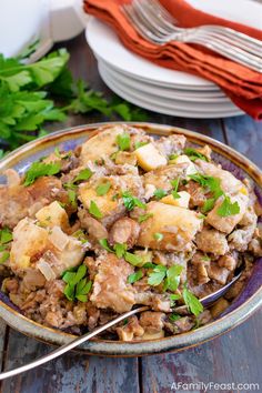 a bowl filled with meat and potatoes on top of a table next to silverware