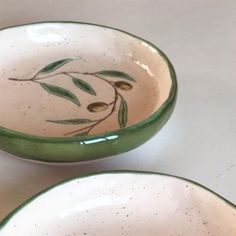 two green and white bowls with olives painted on them sitting on a counter top