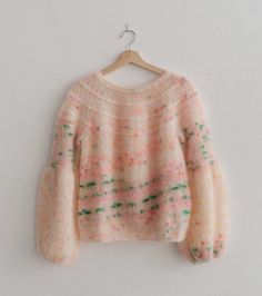 a pink sweater hanging on a hanger next to a white wall with green and pink speckles