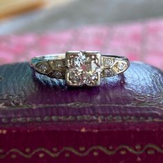 an antique diamond ring sitting on top of a purple leather book with gold trimming