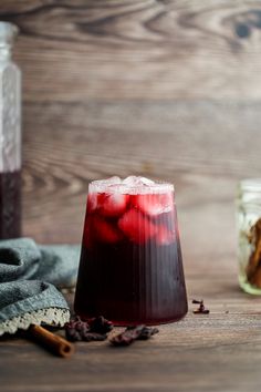 a glass filled with liquid next to two jars and cinnamon sticks on a wooden table