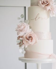 a three tiered wedding cake with pink flowers on top and the word love written on it