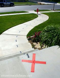 a red cross sitting on the side of a cement road next to a lush green field