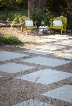 two yellow chairs sitting on top of a stone floor next to grass and trees in the background