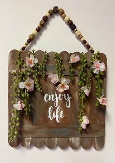 a wooden sign that says enjoy life with flowers hanging on the wall above it is a string of beads