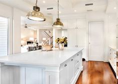 a large white kitchen with wooden flooring and two pendant lights hanging from the ceiling