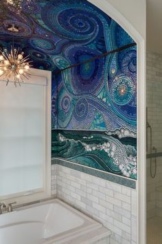 a bath tub sitting under a bathroom window next to a tiled wall covered in blue and white swirls