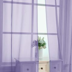 a white vase with flowers sitting on top of a table in front of a window