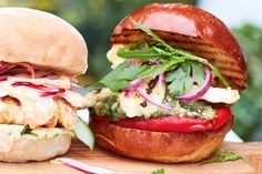 two sandwiches with meat, cheese and veggies sitting on top of a cutting board