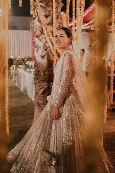 a woman in a wedding dress standing next to a tree with lights on the branches