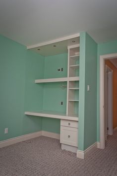 an empty room with blue walls and white shelving unit in the corner on carpeted floor