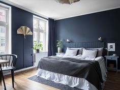 a bedroom with dark blue walls and white bedding is pictured in this image, there are two chairs at the foot of the bed