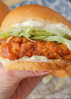 a hand holding a chicken sandwich with lettuce and mayonnaise on it