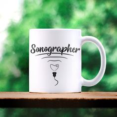 a white coffee mug sitting on top of a wooden table next to a forest filled with green leaves