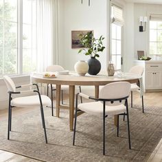 a dining room table with four chairs and a vase on top of it in front of windows