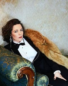 a woman in a tuxedo is sitting on a couch with a teddy bear