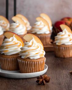 cupcakes with white frosting and apple slices on a plate next to cinnamon sticks