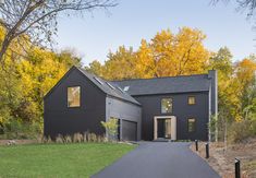 a black house in the fall with yellow and orange trees around it's entrance