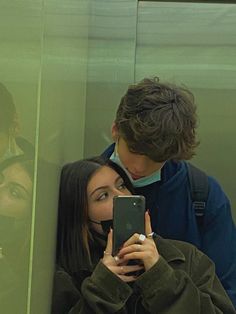 two people standing in front of a mirror looking at their cell phones while one person takes a selfie