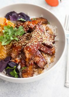 a white bowl filled with rice and meat covered in sesame seeds, garnished with cilantro