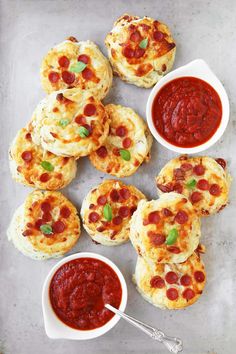 mini pizzas with pepperoni and cheese are on a baking sheet next to small bowls of sauce