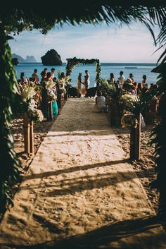 an outdoor ceremony on the beach with lots of people standing around and looking at it