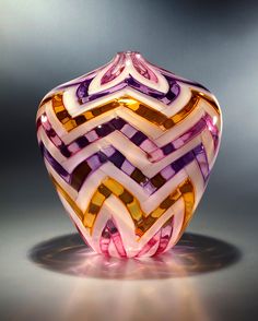 a colorful glass vase sitting on top of a gray table next to a black wall