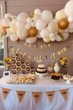 a table topped with lots of desserts next to a wall filled with balloons and honeycombs