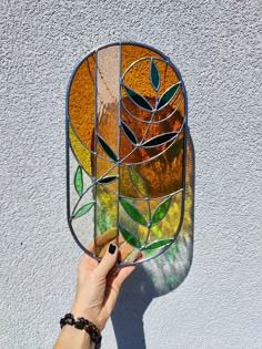 a hand is holding up a stained glass window with leaves on it and the sun shining through