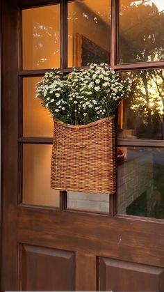 a basket filled with flowers hanging from the side of a wooden door next to a window