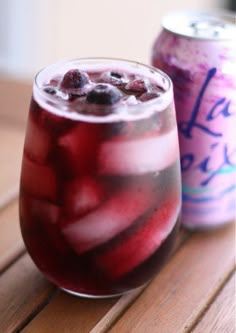 a glass filled with liquid next to a can of soda on top of a wooden table