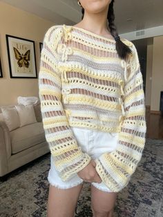 a woman standing in front of a couch wearing white shorts and a yellow knitted sweater