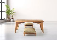 a wooden table with three pillows on it in front of a window and potted plant