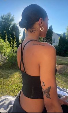 a woman sitting in the grass with tattoos on her back